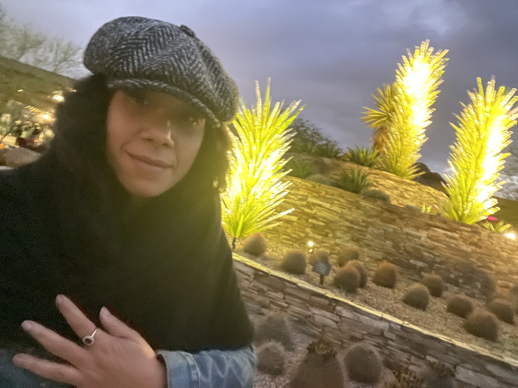 Leah Gillis at the Desert Botanical Garden Christmas light show, standing with a glowing Chihuly glass sculpture under the Arizona night sky.