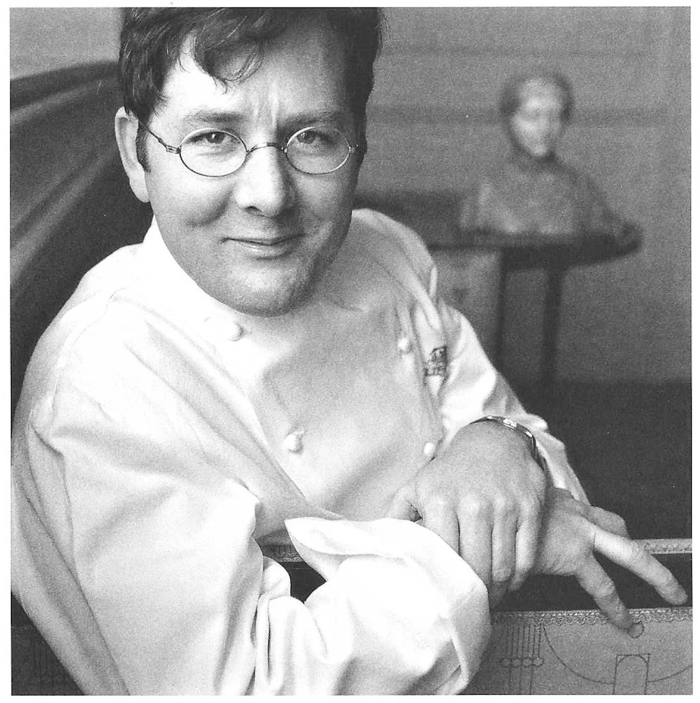 Chef Charlie Trotter smiling in his chef’s smock, showcasing his approachable yet passionate personality in the kitchen. Image source: Charlie-Trotters.com.