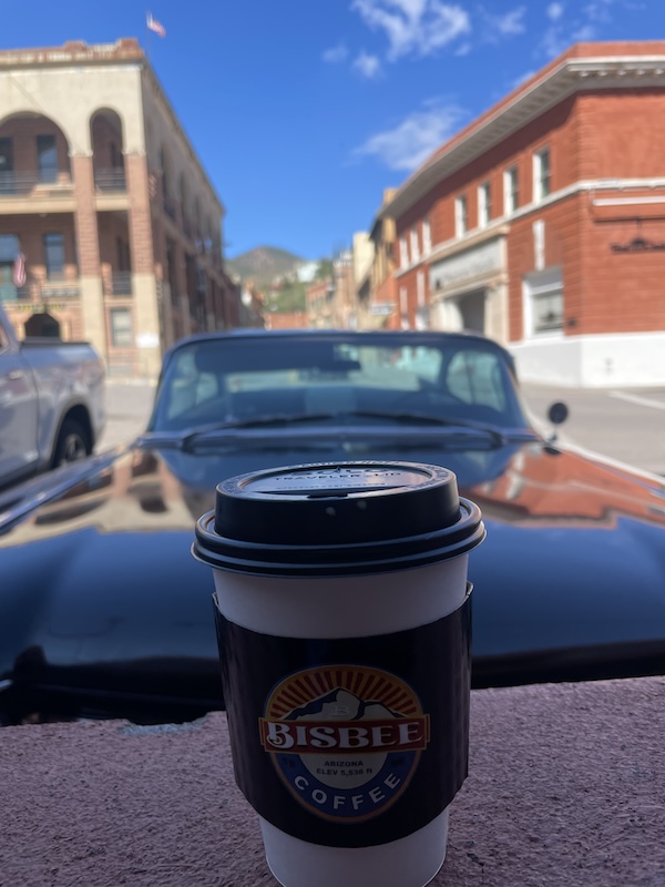 Bisbee Main Street, where vintage cars, mountain air, and a Bisbee Coffee Company cup remind you that time slows beautifully here — history and caffeine keeping pace together.