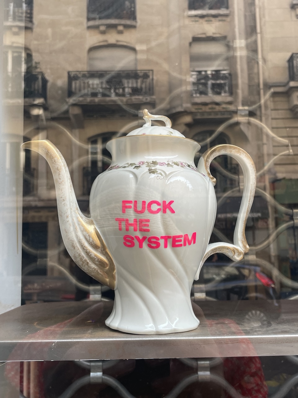 Pink teapot saying fuck the system C'est Extra Montmartre Paris — Gen X Chiron in Aries healing identity astrology 2026