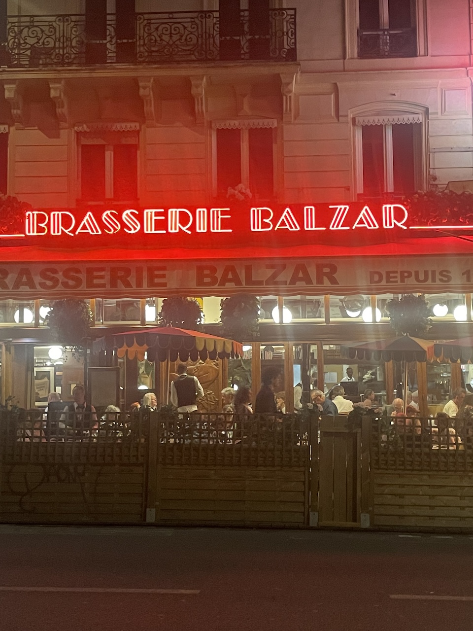 Brasserie Bazaar glowing with neon lights on a Paris street at night.