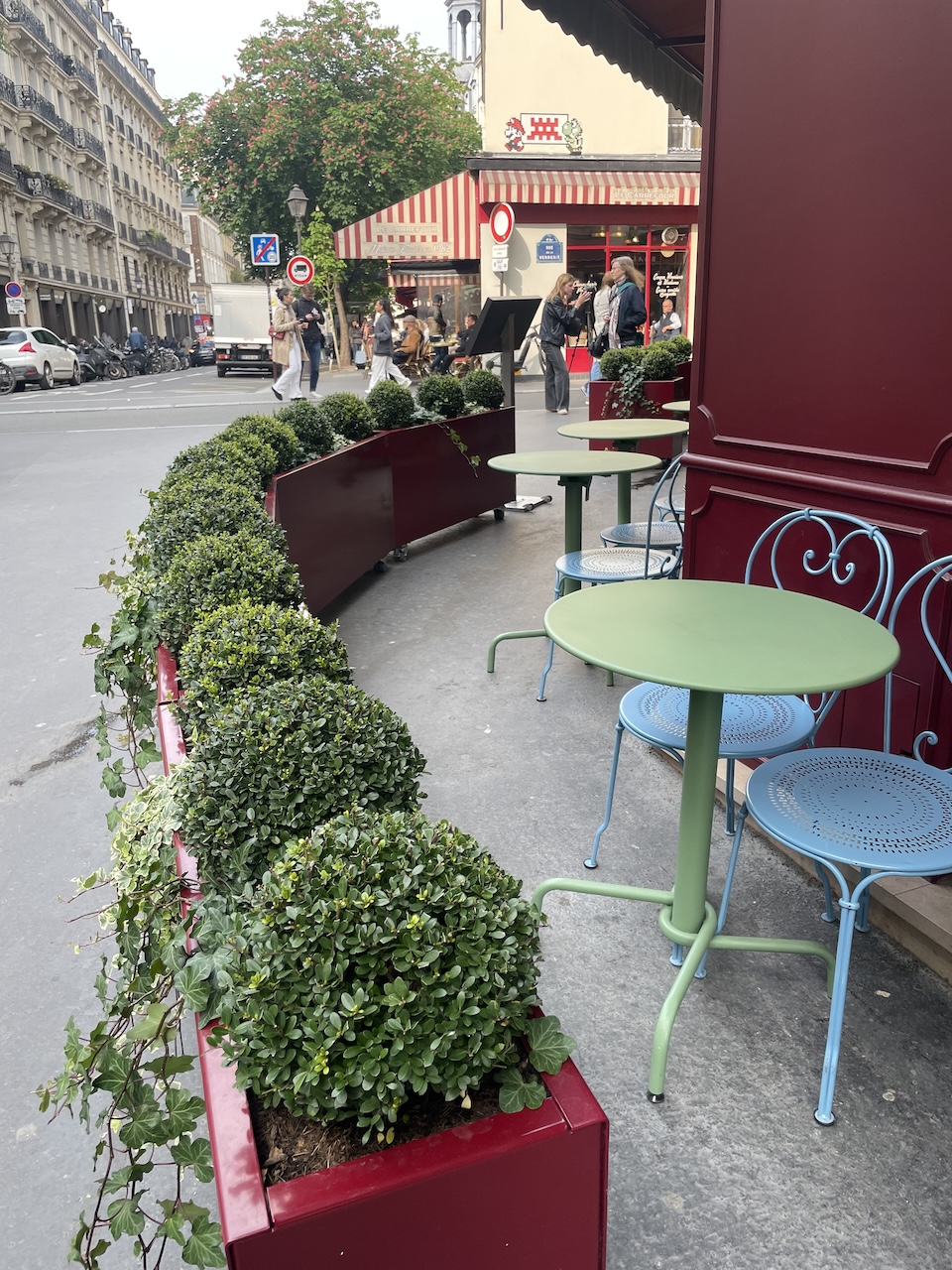 Charming bistro in Le Marais with colorful outdoor seating and greenery along the street.