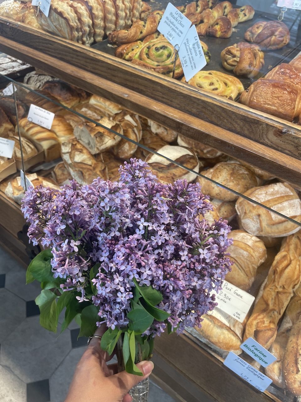 Woman holding a bouquet of lilacs inside a Paris boulangerie.
