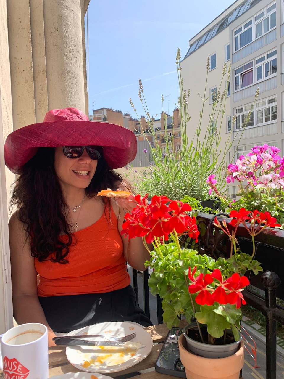 Woman in a wide-brim sun hat enjoying baguette and jam on a lavender-lined Paris terrace with a friend