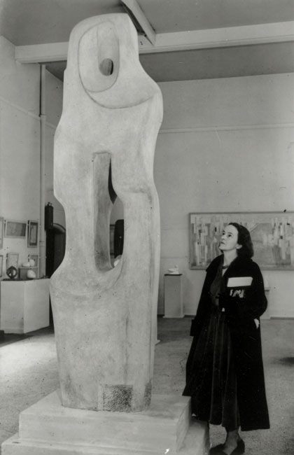 Sculptor Barbara Hepworth standing beside her monumental sculpture Monolith(Empyrean) in a London gallery, 1964.